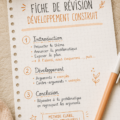 Une femme souriante crée une fiche de révision sur sa table de travail, entourée de fournitures d'étude.